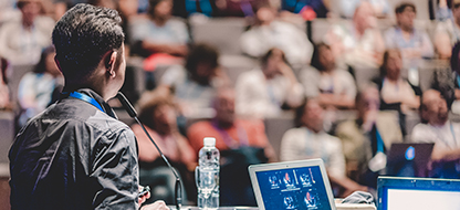 View from behind of a man speaking at a podium to conference attendees