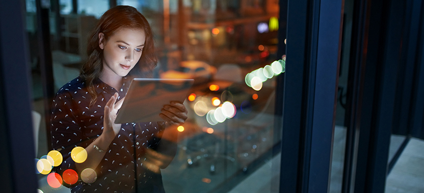woman on a tablet standing in front of a city skyscraper window